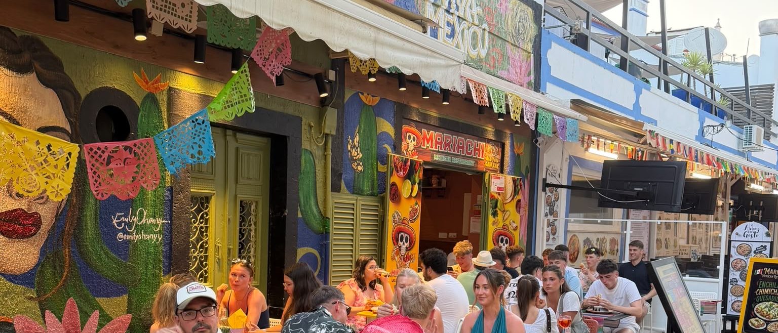 Mariachi's yellow skull sign and papel picado bunting above tables of guests on the cobbled street in Albufeira Old Town