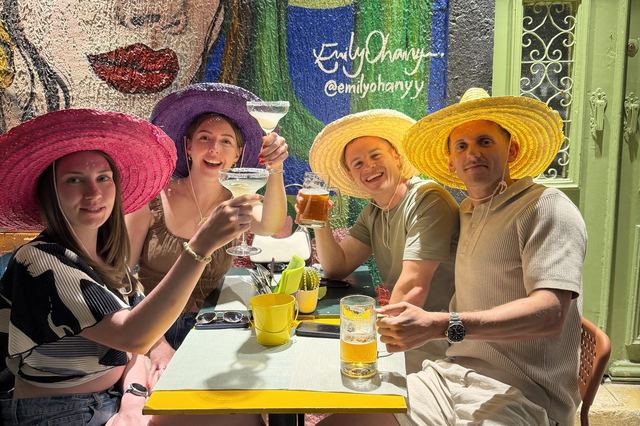 Four guests in straw hats raising margaritas and beer under the Frida mural at Mariachi